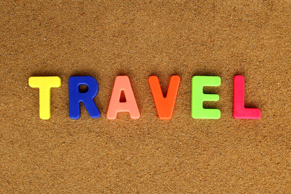 The word `travel` is written on the sand in bright multicolored letters