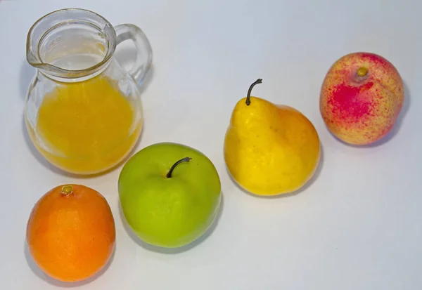 Four fruits, apple, orange, peach,pie, lie diagonally to a glass carafe with freshly squeezed orange juice