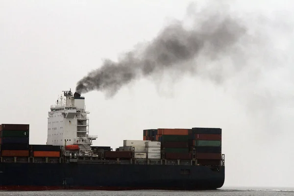 CO2 emisyonları: bir konteyner kargo gemisi beyaz gökyüzüne siyah duman yayıyor
