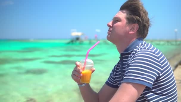 Άνθρωπος πίνοντας κοκτέιλ φρούτων δίπλα στη γαλάζια θάλασσα — Αρχείο Βίντεο