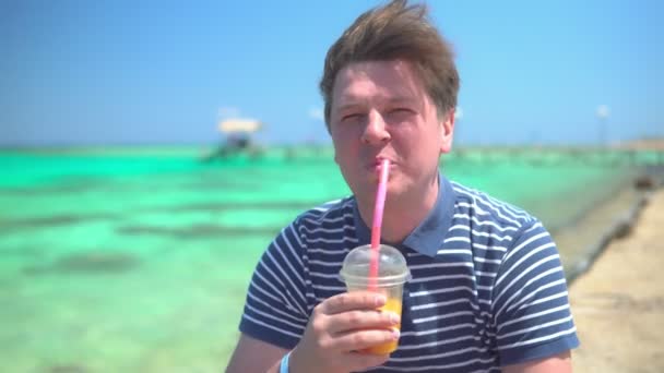 Człowiek pijący koktajl owocowy nad lazurowym morzem — Wideo stockowe