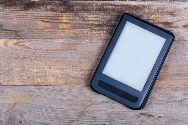 Black e-book reader on wooden background close up