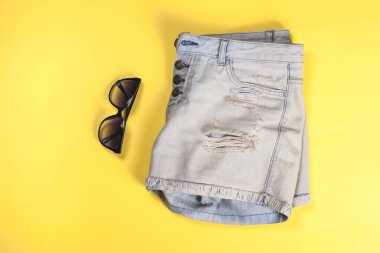 Sarı arka plan ve güneş gözlüklü yıpranmış kadın kot şortu, bir kız için yaz versiyonu.