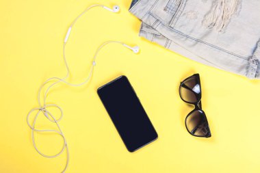 Sarı arka planda beyaz kulaklıklı siyah cep telefonu, yakın plan üst görüntü.