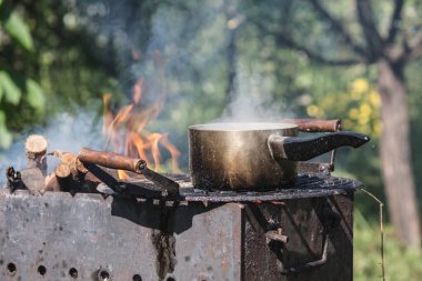 Tarlada ızgarada yuvarlak demir bir tencerede ısıtma suyu. Açık hava yemekleri.