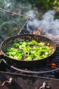 Yanan ateşin üzerinde eski bir demir tavada kızarmış soğan pişirmek. Banliyö bölgesinde yemek pişirme
