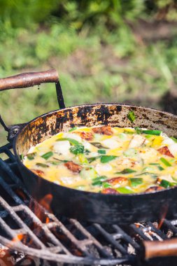Izgarada eski bir demir tavada kıyma ve sebzeyle omlet pişirme süreci..