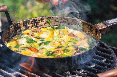 Izgarada eski bir demir tavada kıyma ve sebzeyle omlet pişirme süreci..