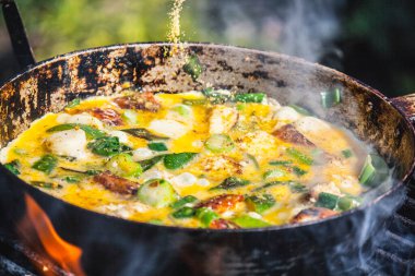 Izgarada eski bir demir tavada kıyma ve sebzeyle omlet pişirme süreci..