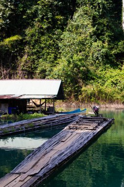 Yoğun tropikal ormanlarla çevrili, sakin, yeşil bir su üzerinde yüzen bir bambu sal, sakin bir kırsal yaşam tarzını ve doğa temelli taşımacılığı yakalıyor..