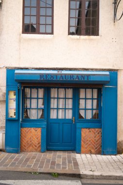 Geleneksel bir Fransız restoranının ön görüntüsü mavi ahşap bir cephe, klasik tabela, küçük camlı pencereler ve tuğla detaylar, düz bir kaldırım taşı caddesinde fotoğraflanmış..