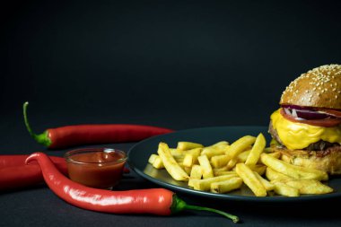 Sosun yanında acı biber ve siyah arka planda patates kızartması ve hamburger.