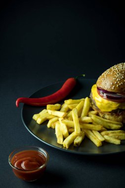 Lezzetli hamburger, patates kızartması ve siyah ketçapın yanında kırmızı biber tabağı.