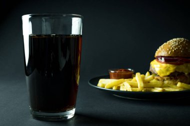 Bir bardak burgerli kola, patates kızartması ve siyah arka planda ketçap.