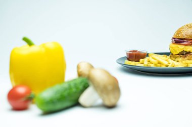 Kızarmış patates ve ketçaplı hamburger. Beyaz arka planda bulanık sebzelerin yanında.