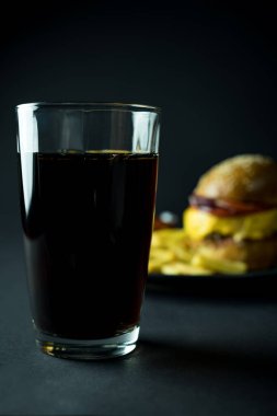 Siyah zemin üzerinde bulanık hamburger olan bir bardak kola.