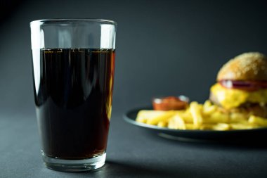 Bulanık hamburgerin yanında kola ve siyah arka planda patates kızartması.