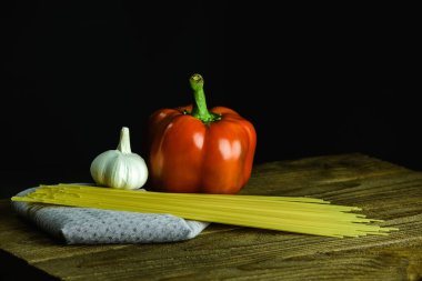 Uncooked spaghetti and garlic with bell pepper on wooden table on black background
