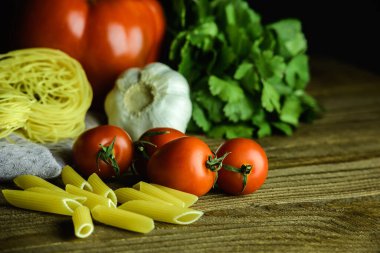 Çiğ makarna ve taze sebzeler ahşap masanın üzerinde.