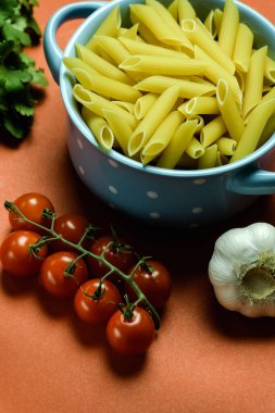 Tabakta çiğ makarna ve kırmızı yüzeyde sebze manzarası.