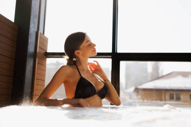 Bikinili esmer kadın jakuzide dinleniyor ve kaplıcada su masajı yapıyor.