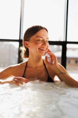Kaplıcadaki jakuzide rahatlayan neşeli bir kadının portresi.