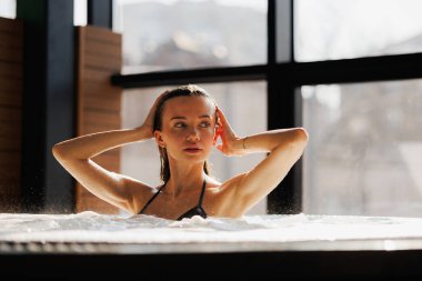 Güzel kadın jakuzide otururken ıslak saçlara dokunuyor.