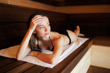 Bikinili esmer kadın saunada bankta yatıyor.