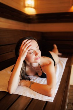 Bikinili rahat bir kadın saunada bankta yatıyor.