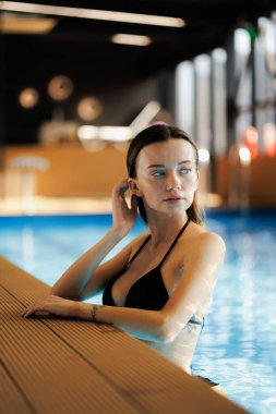 Siyah bikinili bir kadın, spa kompleksinin havuzuna bakıyor.