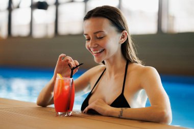 Havuz başında spa kompleksindeki limonataya bakan neşeli bir kadın.