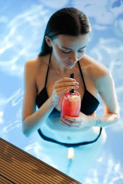 Yüzme havuzunda mavi suyla limonata tutan bikinili bir kadın.