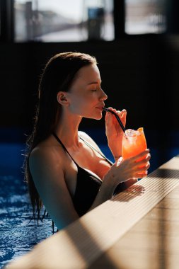 Mayolu kadın, spa kompleksindeki havuz kenarında limonata içiyor.