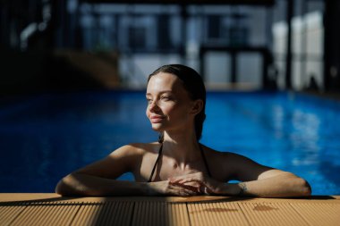 Brunette woman resting at poolside in modern spa center