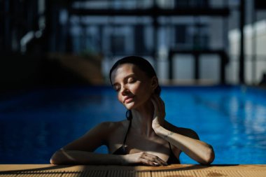 Rahatlamış bir kadın, kaplıcada havuz kenarında gün ışığında dikiliyor.