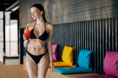 Mayo giymiş rahat bir kadın spa kompleksinde kokteyl tutuyor.