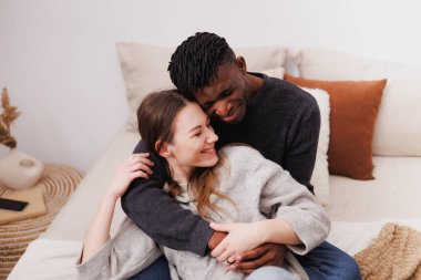 Mutlu Afrikalı Amerikalı adam evinde yatakta neşeli kız arkadaşına sarılıyor.