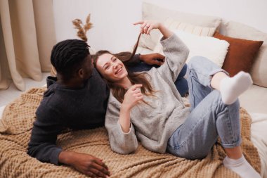 Gülümseyen kadın yatakta yatarken Afrikalı Amerikalı erkek arkadaşıyla konuşuyor.