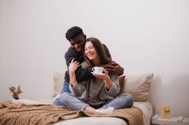 Pozitif Afro-Amerikalı bir adam evde kahve fincanı ile kız arkadaşına sarılıyor.