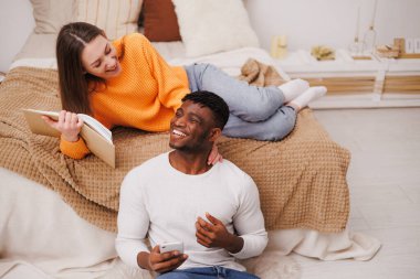 Afro-Amerikan erkek arkadaşının yanında elinde kitapla gülümseyen bir kadın.