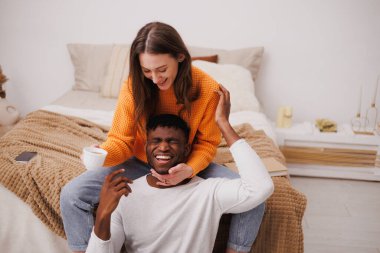 Gülümseyen kadın kahve fincanı tutuyor ve Afrikalı Amerikalı erkek arkadaşına sarılıyor.