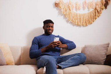 Gülümseyen Afro-Amerikan atlamacı. Akşamları koltukta akıllı telefon kullanıyor.