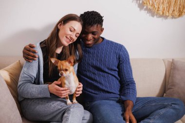 Gülümseyen ırklar arası bir çift oturma odasında chihuahua köpeğiyle vakit geçiriyor.
