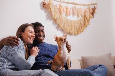 Mutlu çoklu etnik çiftler kanepede köpekle vakit geçiriyor.