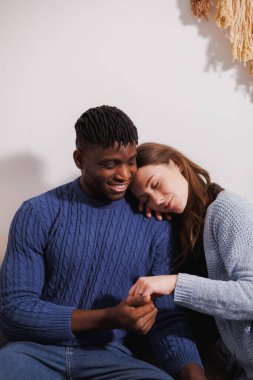 Gülümseyen Afrikalı Amerikalı bir adam akşam evde kız arkadaşının elini tutuyor.