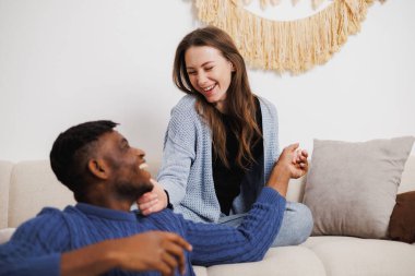 Gülümseyen kadın oturma odasında Afrikalı Amerikalı erkek arkadaşıyla vakit geçiriyor.