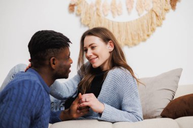Gülümseyen kadın, evdeki kanepede Afro-Amerikan erkek arkadaşının elini tutuyor.