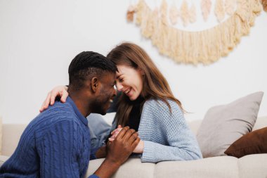 Evdeki koltukta el ele tutuşan neşeli ırklar arası bir çift.