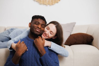Gülümseyen kadın evdeki kanepede Afro-Amerikan sevgilisine sarılıyor.