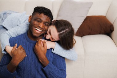 Gülümseyen kadın oturma odasında Afrikalı Amerikalı sevgiliye sarılıyor.